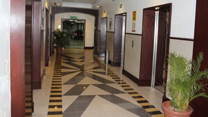 Un pasillo de hotel con piso de diseño geométrico, puertas y plantas en macetas.