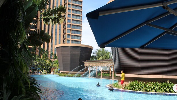 Una piscina con gente, un elemento acuático y un edificio moderno con fachada curva.