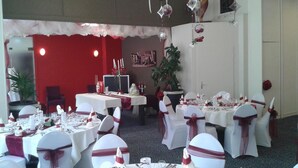 Un salón de banquetes con mesas redondas, manteles blancos y sillas con lazos rojos.