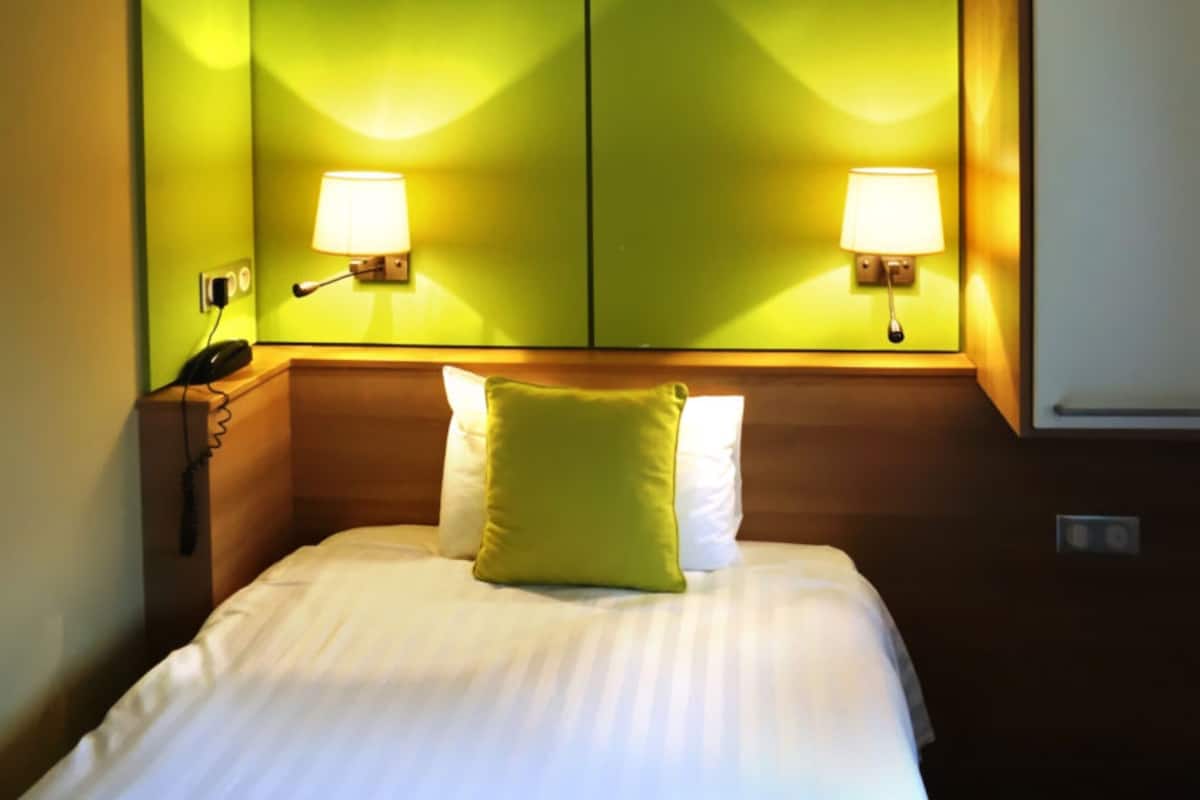 A hotel room with a bed, two bedside lamps, and a telephone on the nightstand.