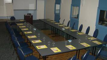 Une salle de conférence avec de longues tables, des chaises bleues et un tableau blanc.