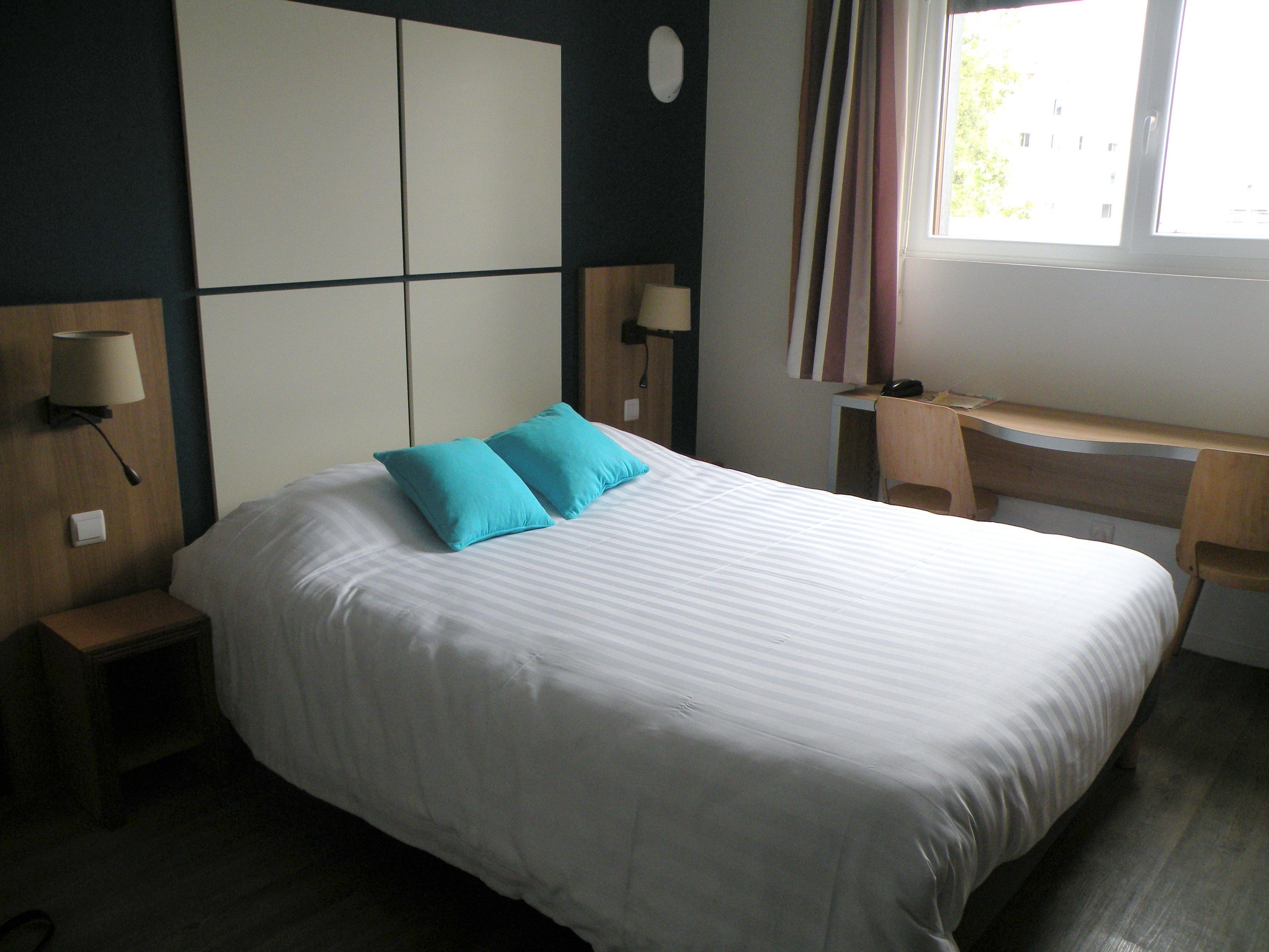 Ein Hotelzimmer mit einem großen Bett, zwei Nachttischlampen, einem Schreibtisch und einem Fenster mit Vorhängen.
