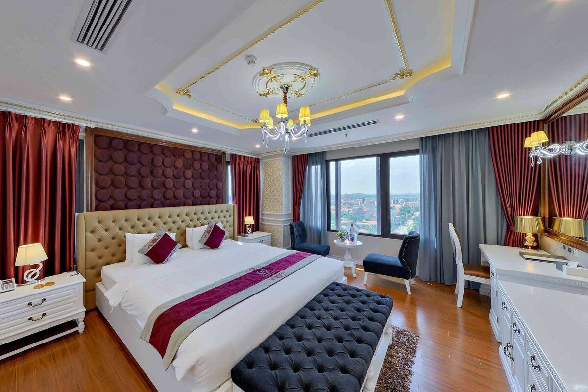 A spacious hotel room with a large bed, a sitting area, and a view of the city.