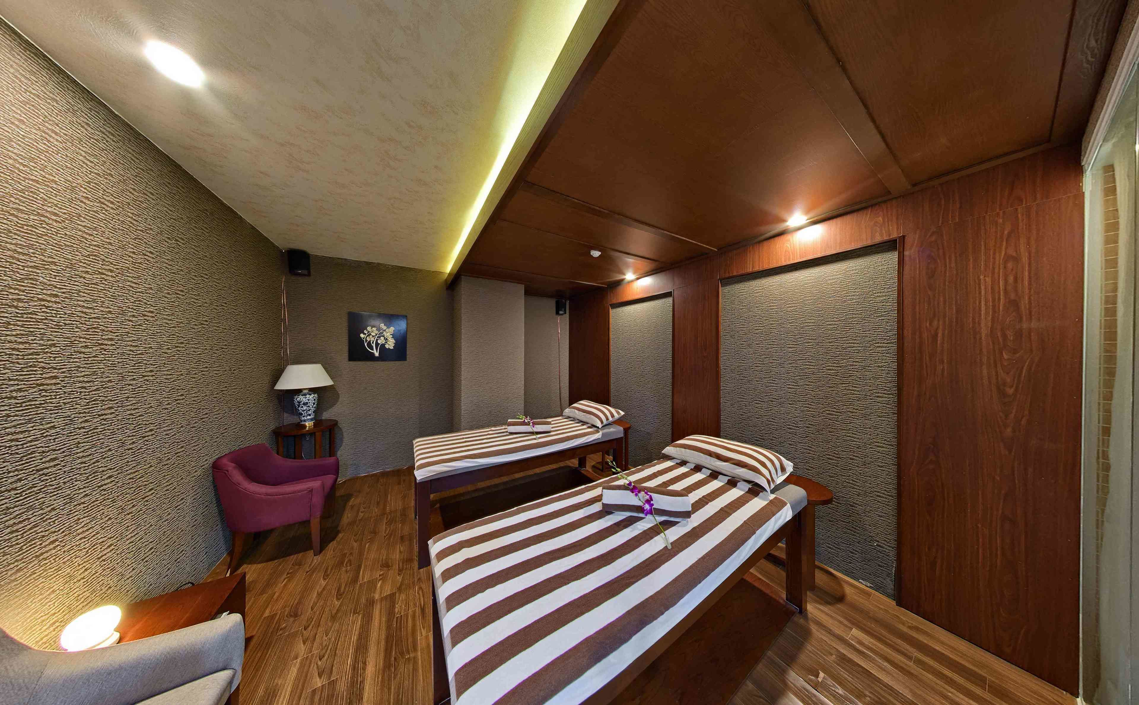 Ein Zimmer mit zwei Betten, einem kleinen Tisch, einem Stuhl und einer Wandlampe.