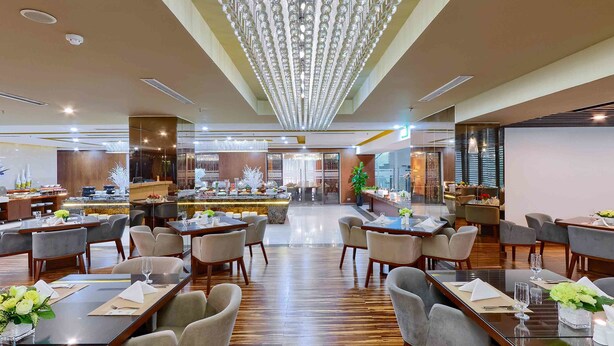 Ein geräumiges Restaurant mit mehreren Essbereichen, einer zentralen Bar und einem modernen Kronleuchter.