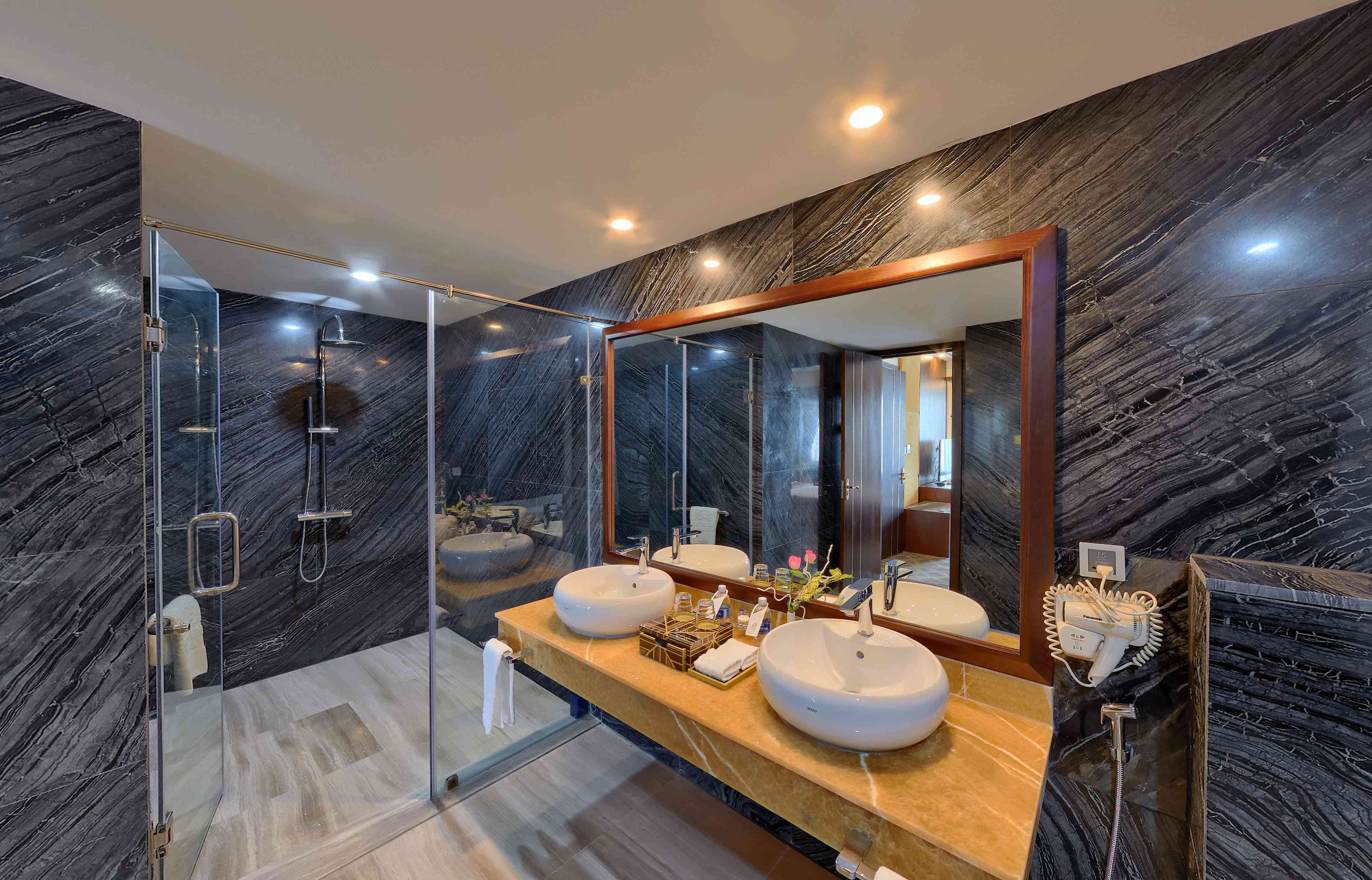 Een moderne badkamer met een douche met glazen wand, twee wastafels en een grote spiegel.