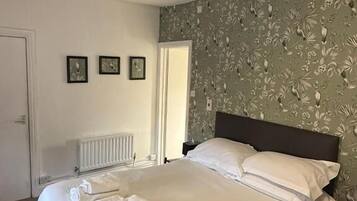 Una cama bien hecha con sábanas y toallas blancas, un radiador, una puerta y una pared con estampado floral.