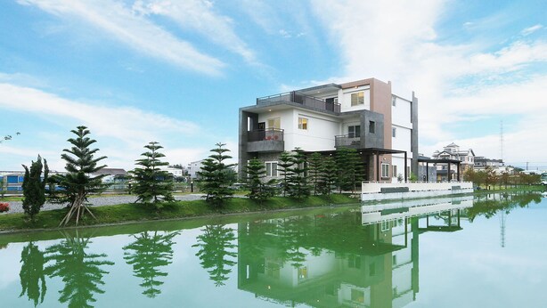 A modern two-story building with a balcony, surrounded by a calm water body and greenery. - Langkawi Garden B&B (Luodong)