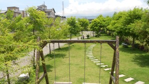 A wooden swing set in a grassy area with a clear view of houses and a body of water in the background. - Langkawi Garden B&B (Luodong)