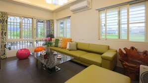 A modern living room with a green sofa, a glass coffee table, and a large window with a view of greenery. - Langkawi Garden B&B (Luodong)