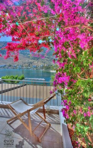 Een balkon met uitzicht op een meer en bergen, houten stoelen en roze bougainvillea bloemen.