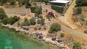 Un hotel costero con varias construcciones, vista despejada al mar y un estacionamiento con sombrillas.