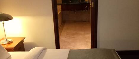 A hotel room with a bed, a bedside lamp, a bathroom visible through an open door, and a mirror with lights.