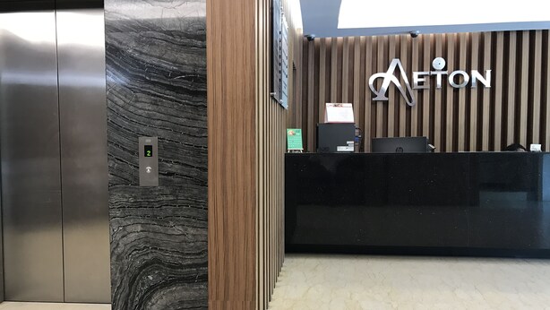 A reception desk with a wooden panel background and a sign that reads "AETON". - Aeton Hotel (Nilai)