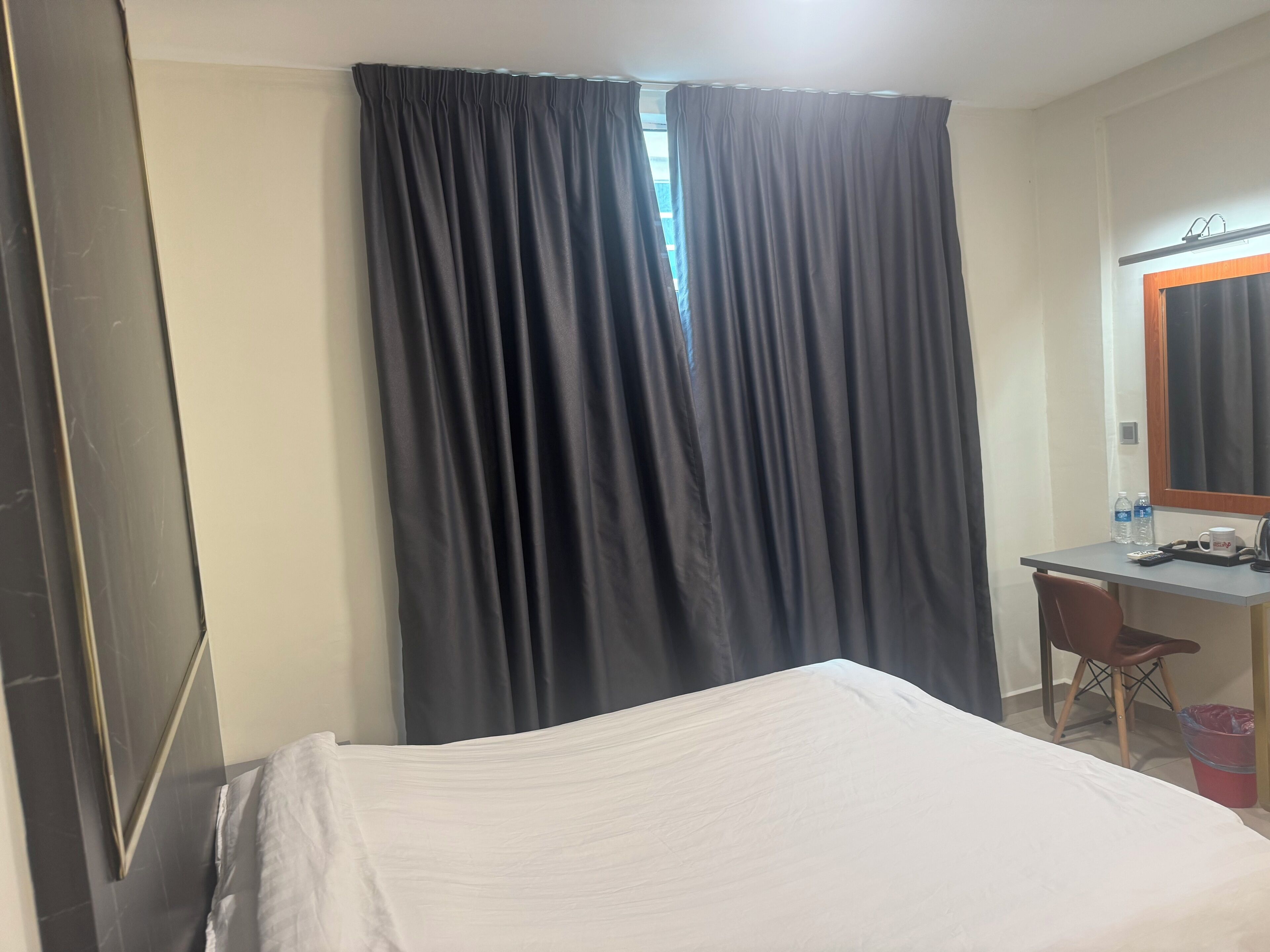 Habitación de hotel con cama, escritorio, silla, espejo y ventana con cortinas.