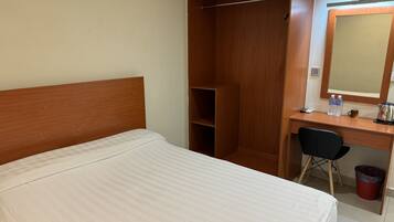 A hotel room with a bed, a desk with a chair, a wardrobe, and a mirror.