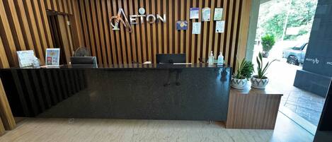 Un mostrador de recepción de hotel con un panel de madera de fondo, una encimera negra y vistas al exterior.