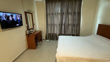 A hotel room with a bed, a desk with a chair, a television mounted on the wall, and a large window with curtains.