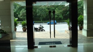 A hotel entrance with a glass door, potted plants, and a visible street with parked cars and a motorcycle. - Aeton Hotel (Nilai)