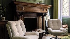 Een kamer met twee fauteuils, een open haard en een raam met gordijnen.