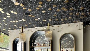 A bar area with a marble countertop, green bar stools, and shelves stocked with bottles. - Hôtel des Quinconces (Bordeaux)