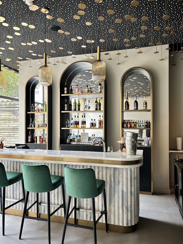 A bar area with a marble countertop, green bar stools, and shelves stocked with bottles. - Hôtel des Quinconces (Bordeaux)