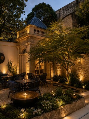 An outdoor dining area with tables and chairs, a fountain, and a stone wall. - Hôtel des Quinconces (Bordeaux)