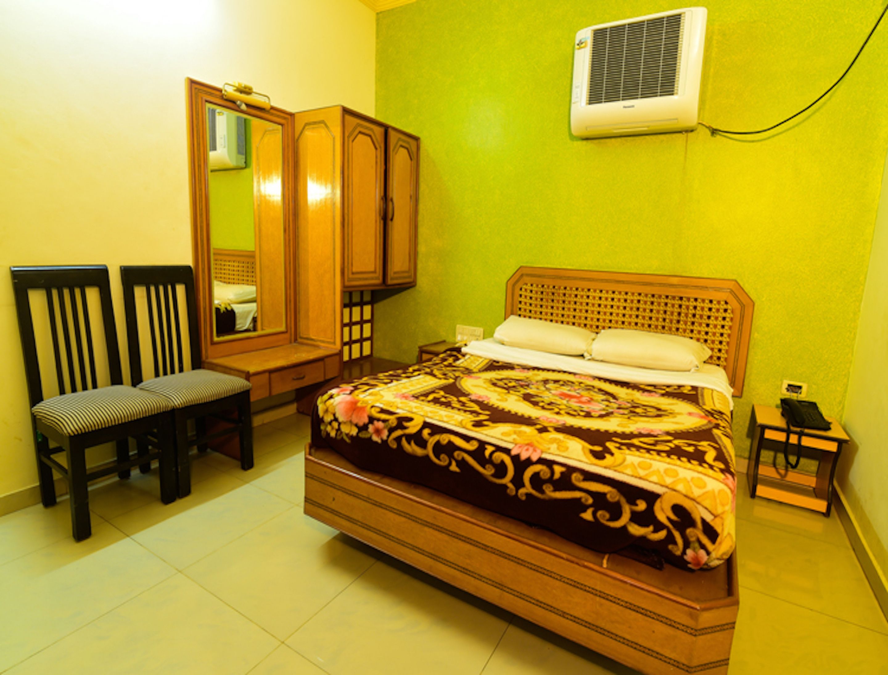 A bedroom with a bed, two chairs, a wardrobe, and a bedside table.