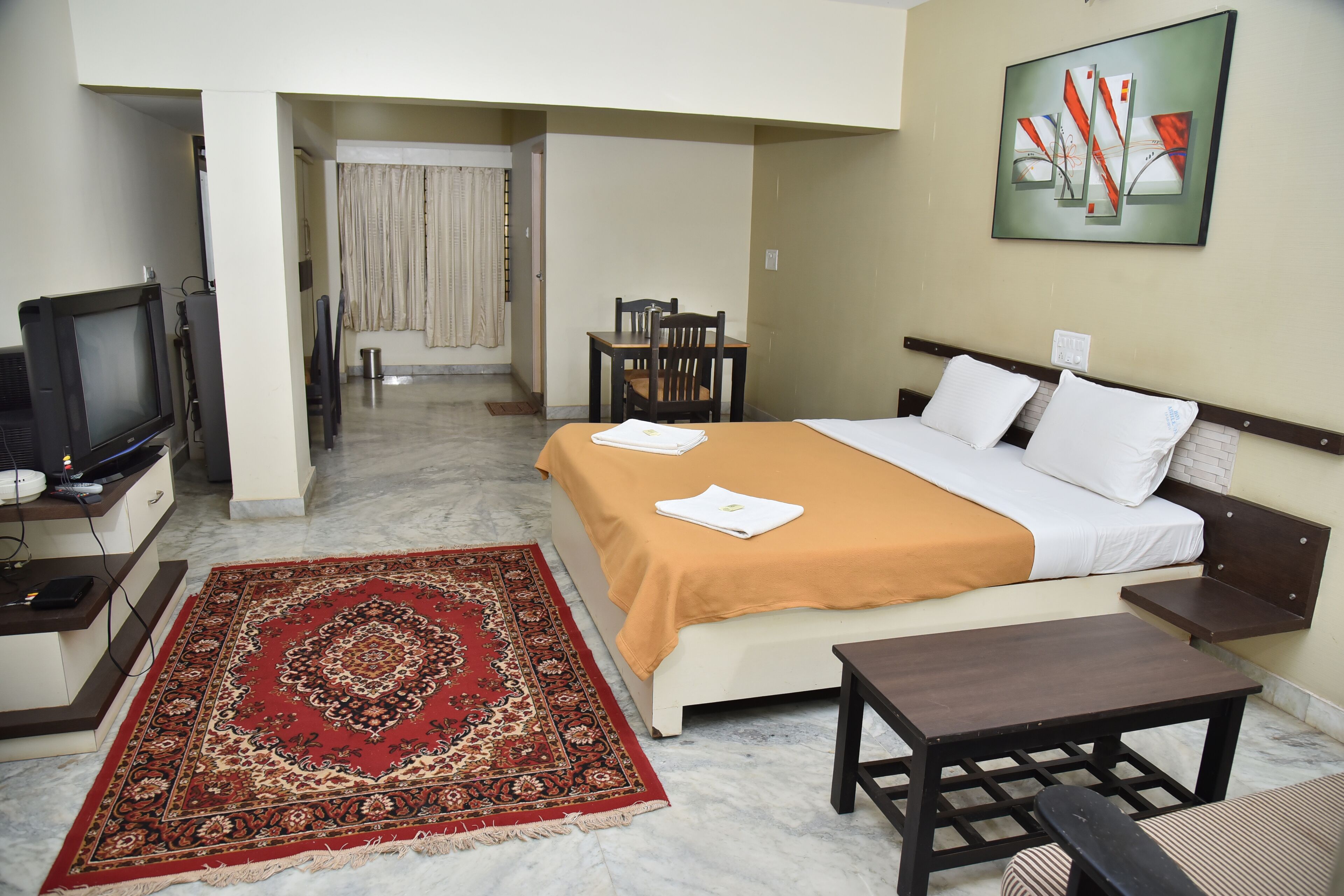 A hotel room with a bed, a desk, a television, a chair, and a rug.