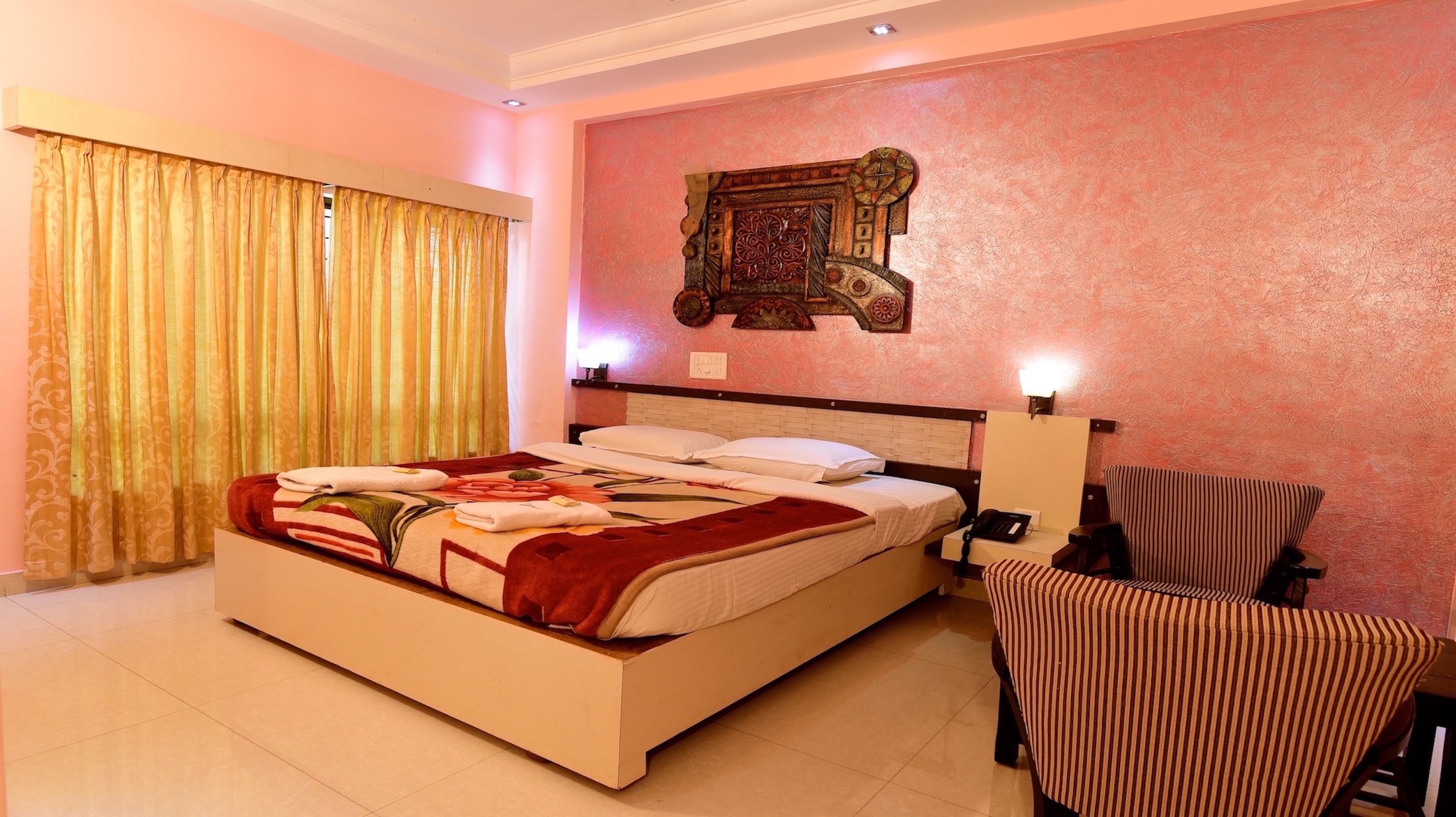 A hotel room with a bed, a bedside table with a lamp, a chair, and a decorative wall piece.