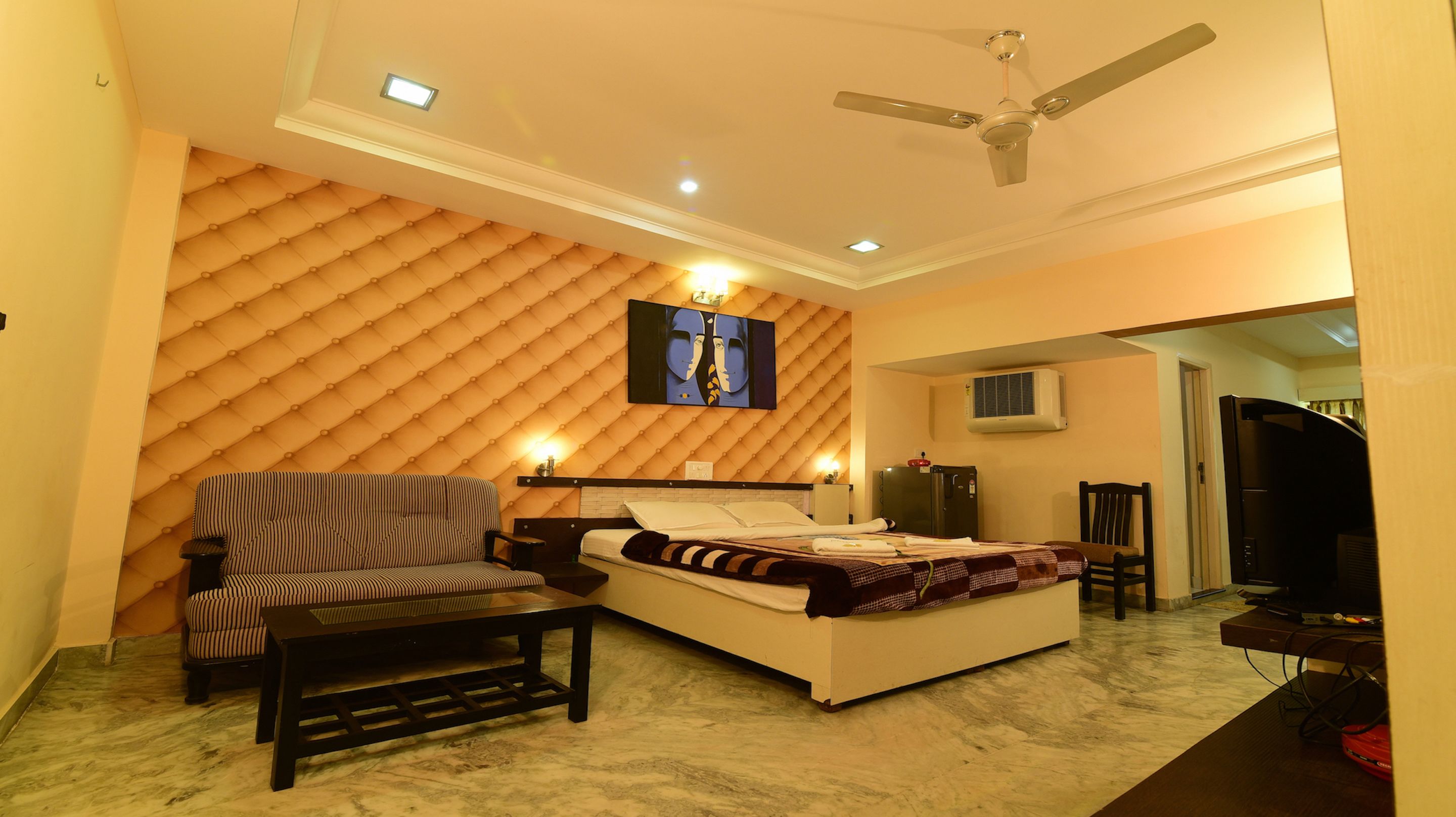 A bedroom with a bed, a sofa, a TV, and a ceiling fan.