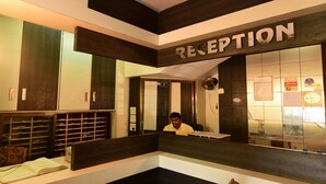 Un área de recepción con un espejo grande que refleja el interior, un mostrador de recepción y una pared con un tablón de anuncios.