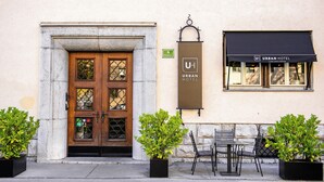 Entrada de hotel con puertas dobles, un letrero que indica una calificación de 4 estrellas, asientos al aire libre con sillas y mesas, y un letrero colgante del Urban Hotel.