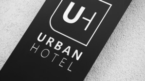 Un letrero negro con texto blanco que dice "URBAN HOTEL" y un cuadrado blanco con una "U" mayúscula en su interior.