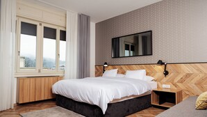 Un dormitorio con cama, mesita de noche, lámpara de pared, espejo y ventana con cortinas.