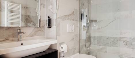 A bathroom with a white sink, a toilet, a glass shower enclosure, and a towel rack.