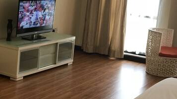 A hotel room with a television on a cabinet, a bed, a window with curtains, and a wicker chair.