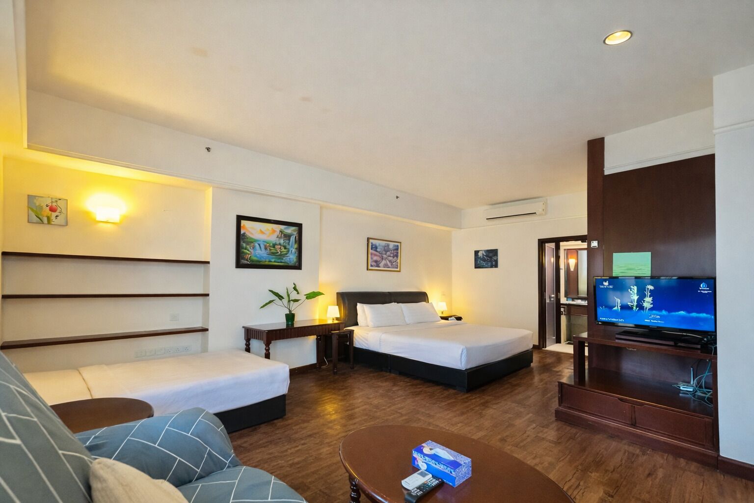 Habitación de hotel con dos camas, un sofá, un televisor y una mesita con un control remoto.