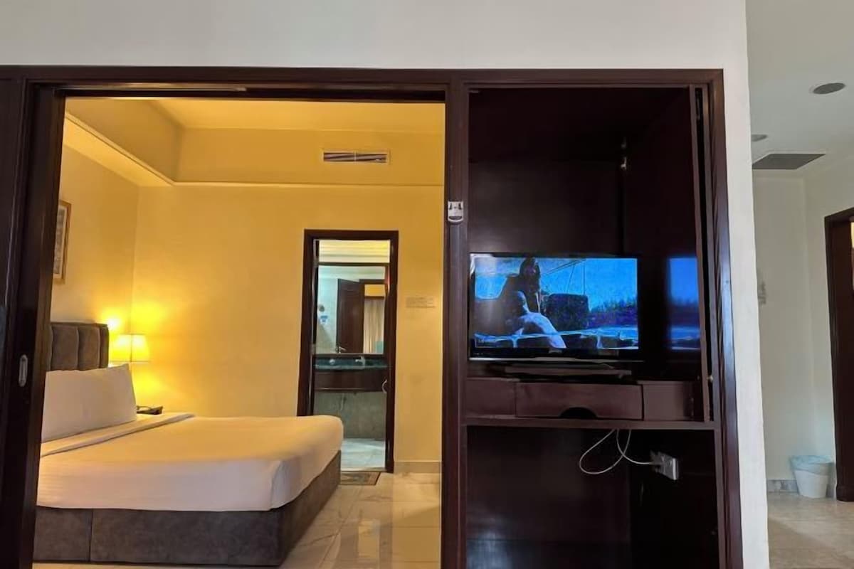 A hotel room with a bed, a TV, and a bathroom visible through an open door.