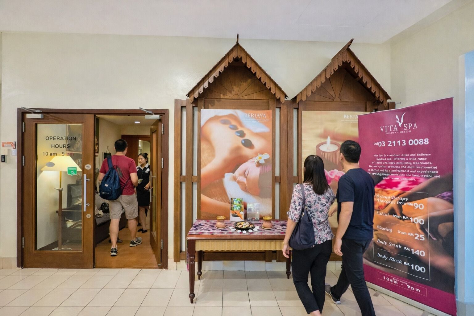 A spa area with a wooden reception desk, a poster advertising services, and a door with operation hours.
