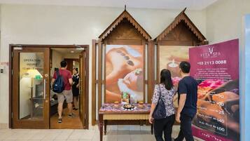 A spa area with a wooden reception desk, a poster advertising services, and a door with operation hours.