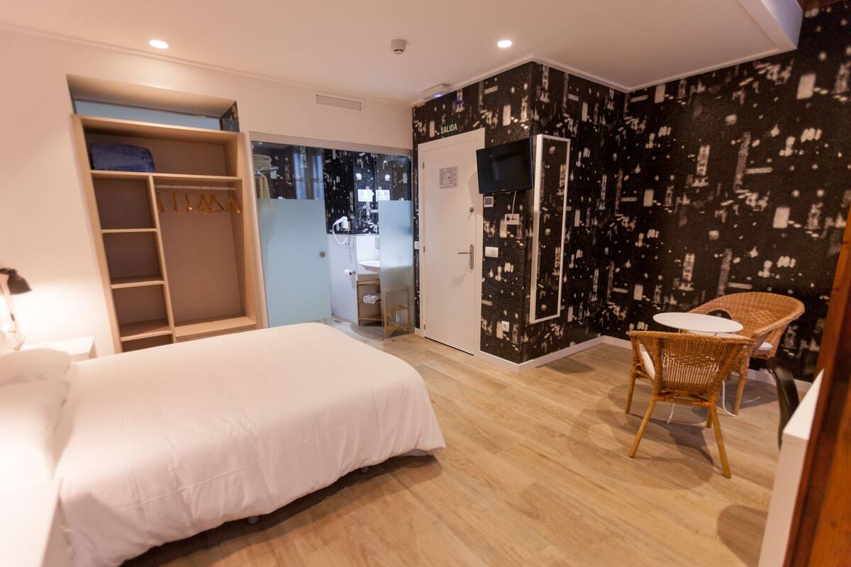 A bedroom with a bed, a wardrobe, a mirror, and a small table with chairs.