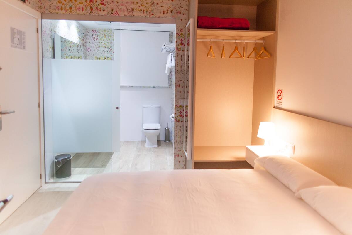 A hotel room with a bed, a bathroom with a toilet and a shower, and a closet with hangers.