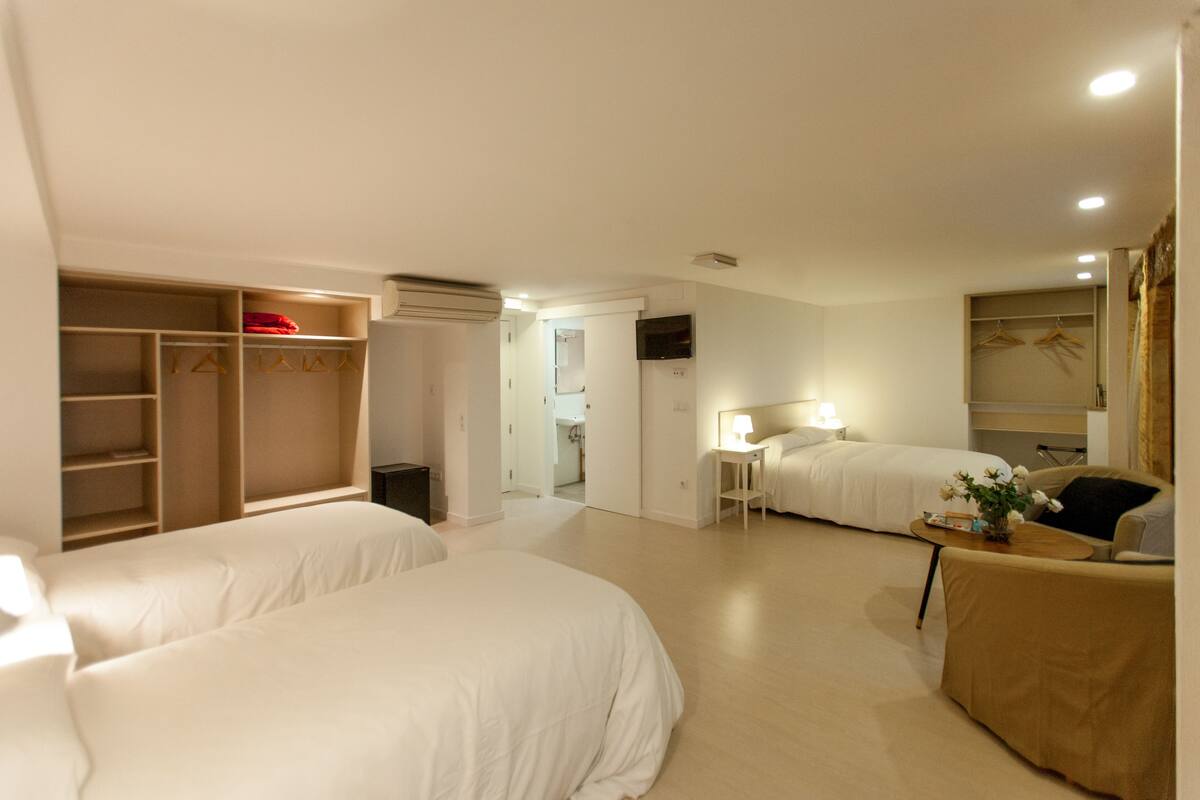 A hotel room with two beds, a seating area, a wardrobe, and a television.