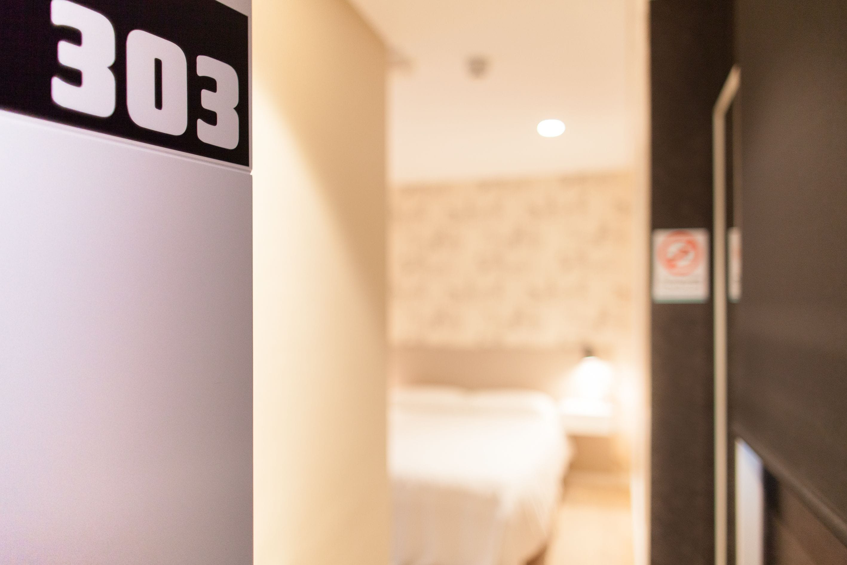 A hotel room with a bed, a nightstand, and a wall-mounted sign displaying the number 303.