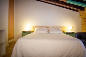 Ein ordentlich bezogenes Bett mit weißen Leinen in einem Zimmer mit Holzbalkendecke und Backsteinwand. Es gibt zwei Nachttische mit Lampen.