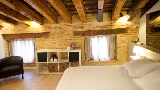 A room with exposed wooden beams, a brick wall, a bed, a sofa, a TV, and a small table with a lamp. - Host & Home (Valencia)