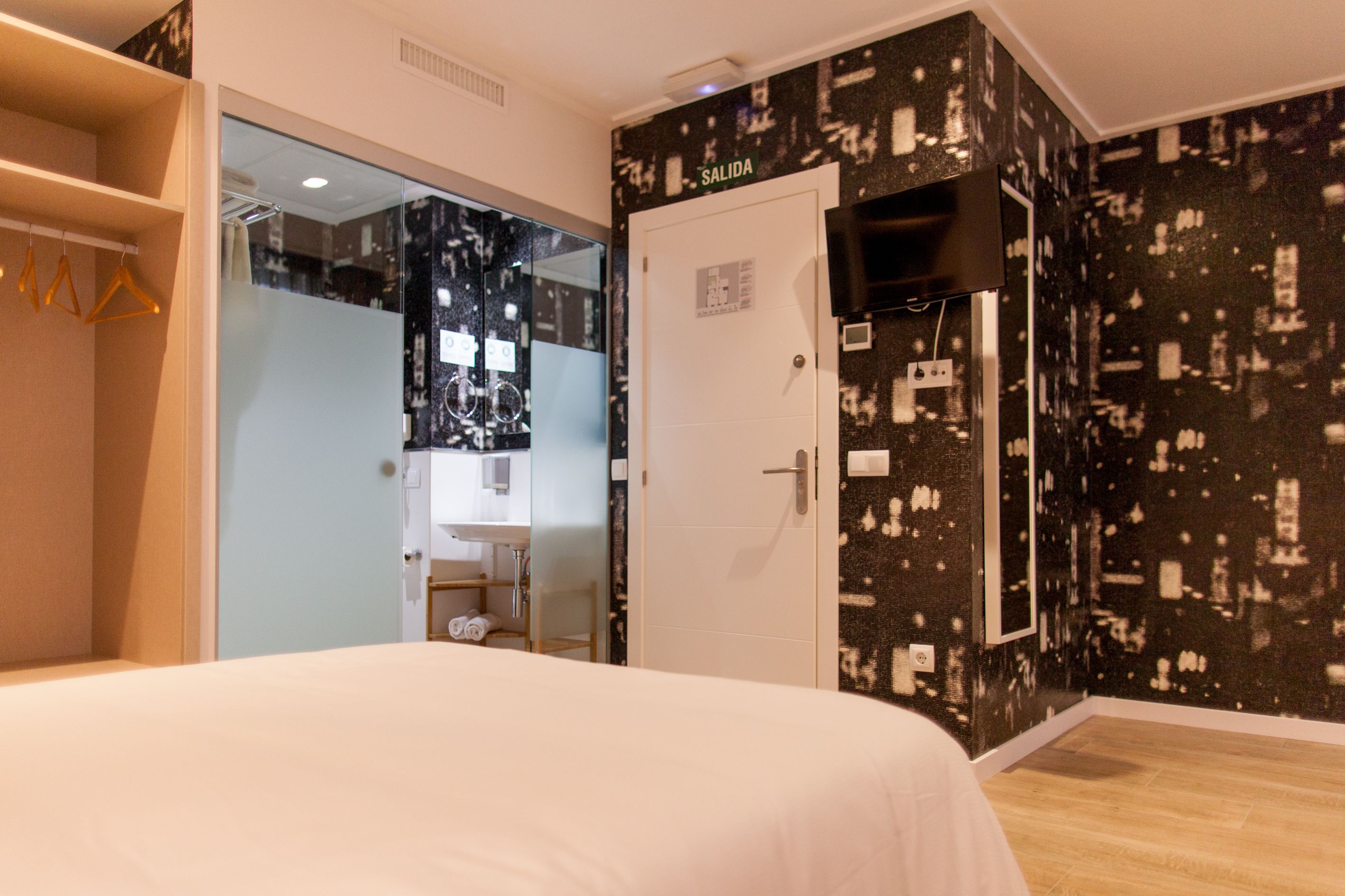 Habitación de hotel con cama, armario, baño con espejo y pared con cartel que indica 'SALIDA'.