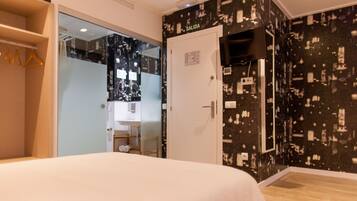 Habitación de hotel con cama, armario, baño con espejo y pared con cartel que indica 'SALIDA'.