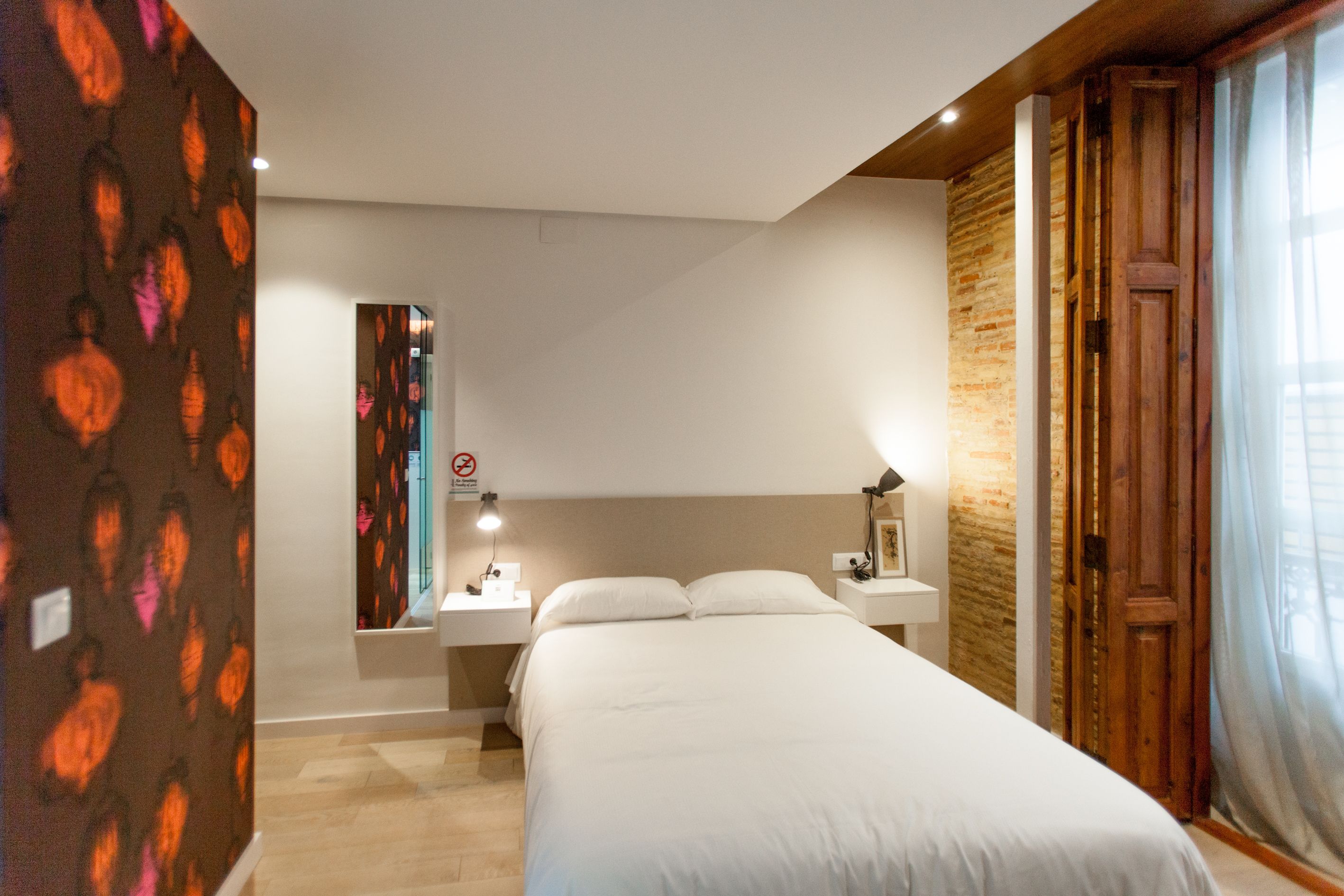 A hotel room with a bed, bedside tables, a mirror, and a wooden door.